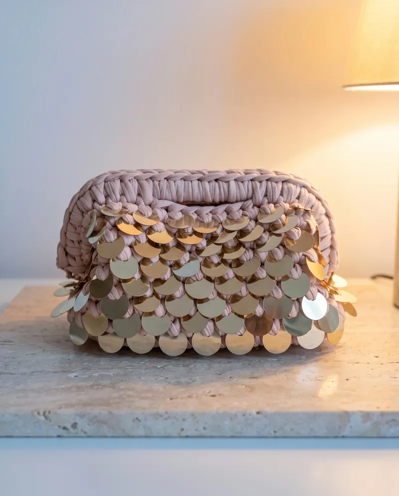 Clutch cipria all'uncinetto con paillettes dorate su un davanzale al tramonto