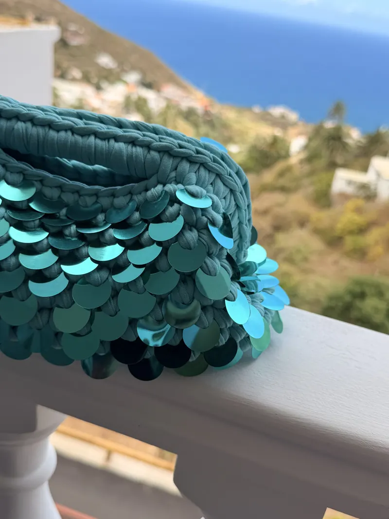 Clutch turchese con maxi paillettes su un balcone con vista sul mare